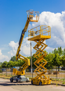 Yellow Scissors lift and boom lift parked outdoors